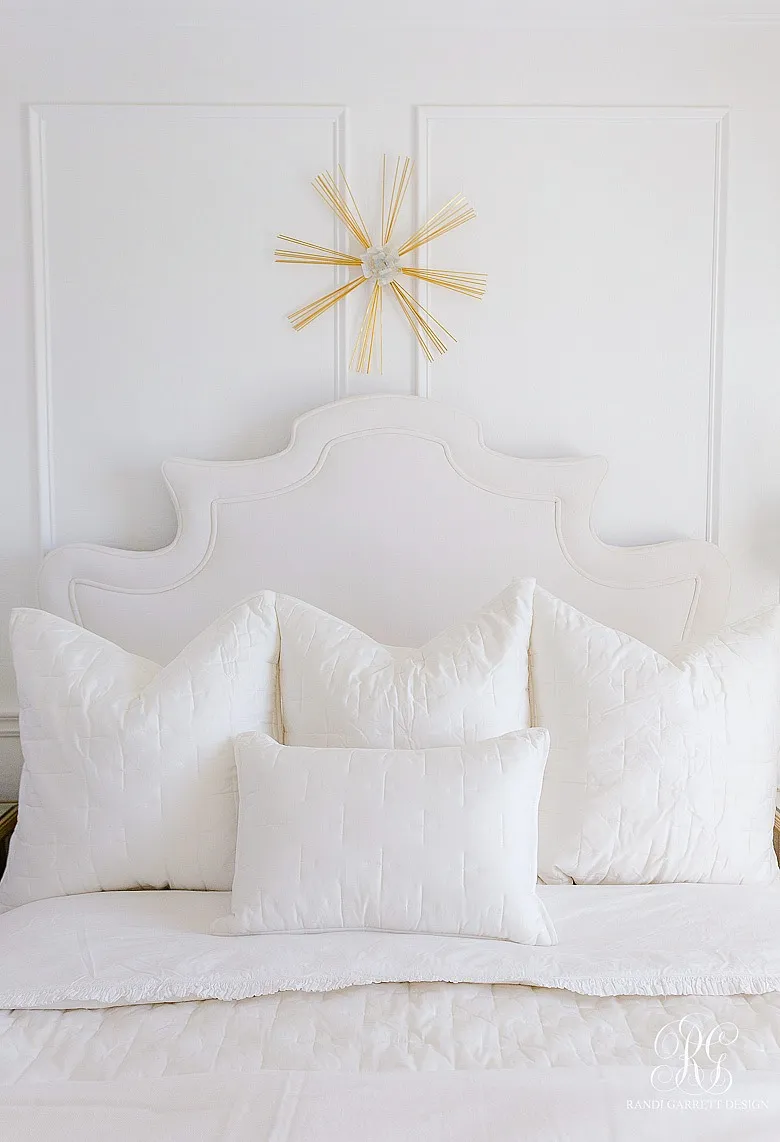 A queen-sized bed styled with white quilted Euro pillows and a single lumbar pillow.