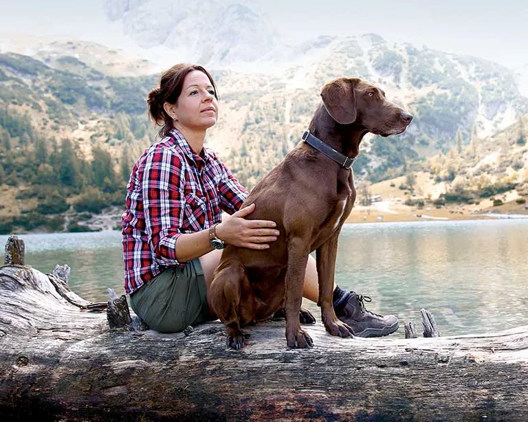 Man with dog at a lake sitting on a fallen tree.