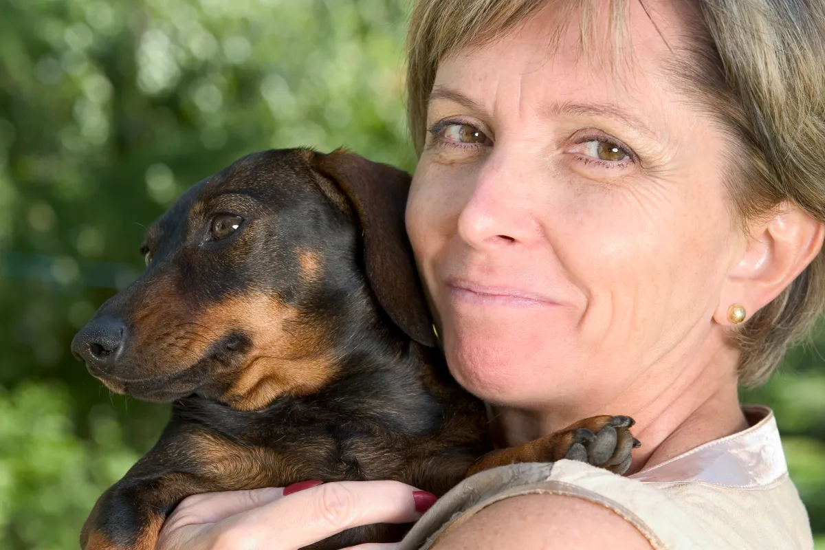 Mature woman smiling warmly while holding a small white dog, representing the ideal Wag dog walker profile image