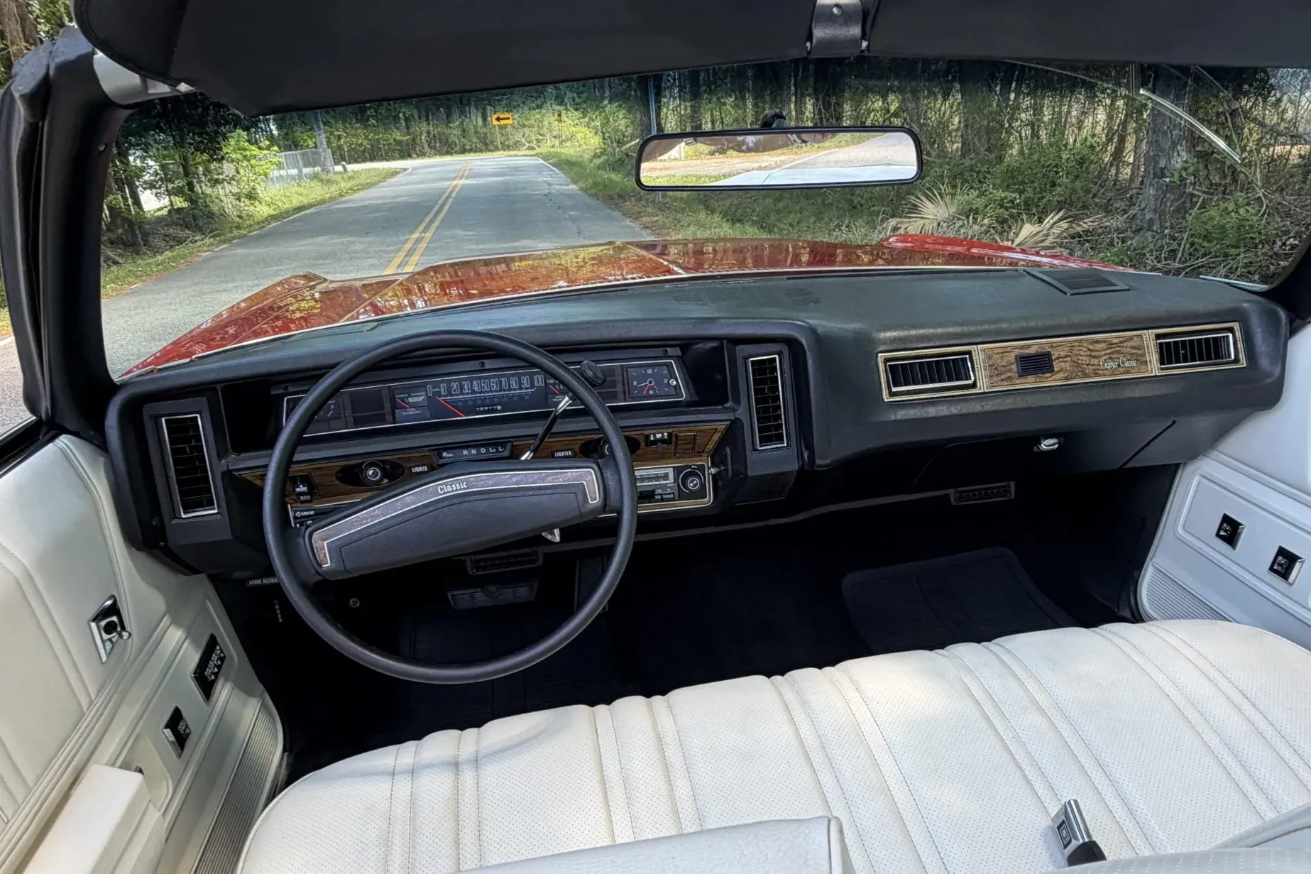 White vinyl interior with bench seat, woodgrain dashboard trim, and classic luxury features