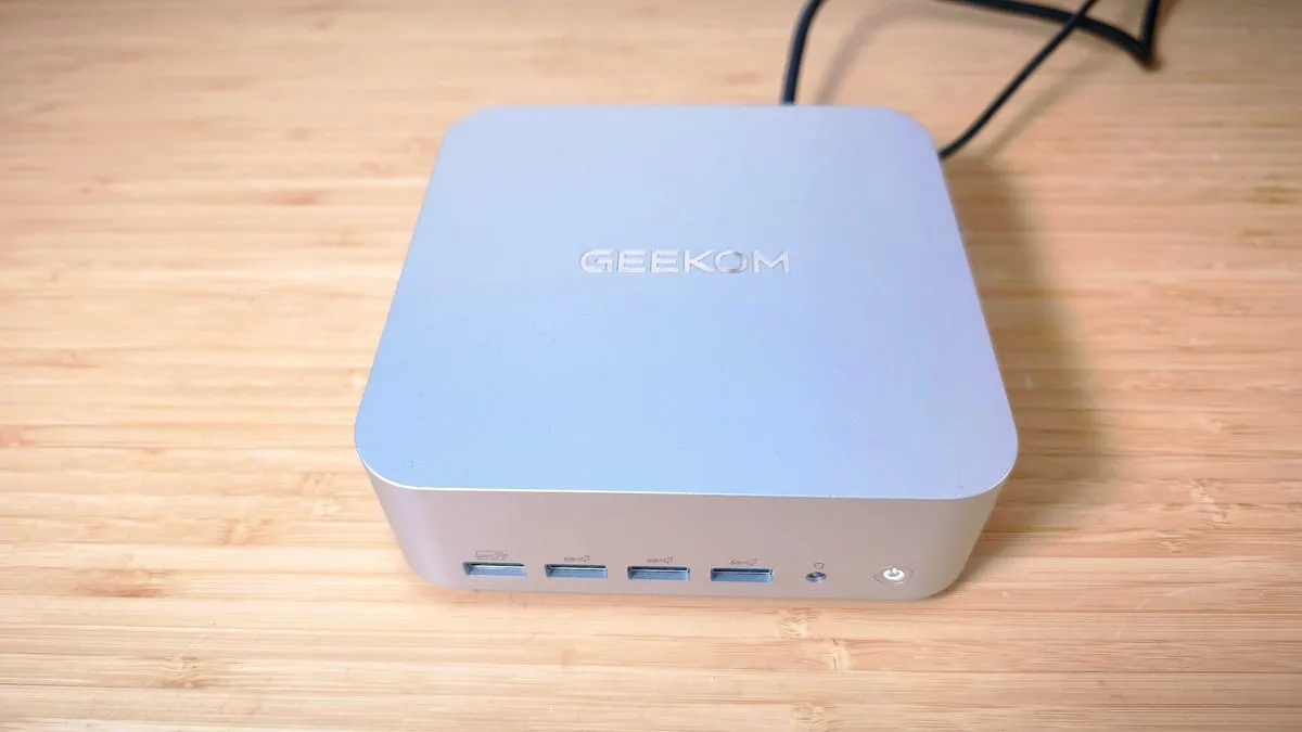 A compact silver Geekom A9 Max mini PC on a wooden desk, highlighting its minimalist and functional design