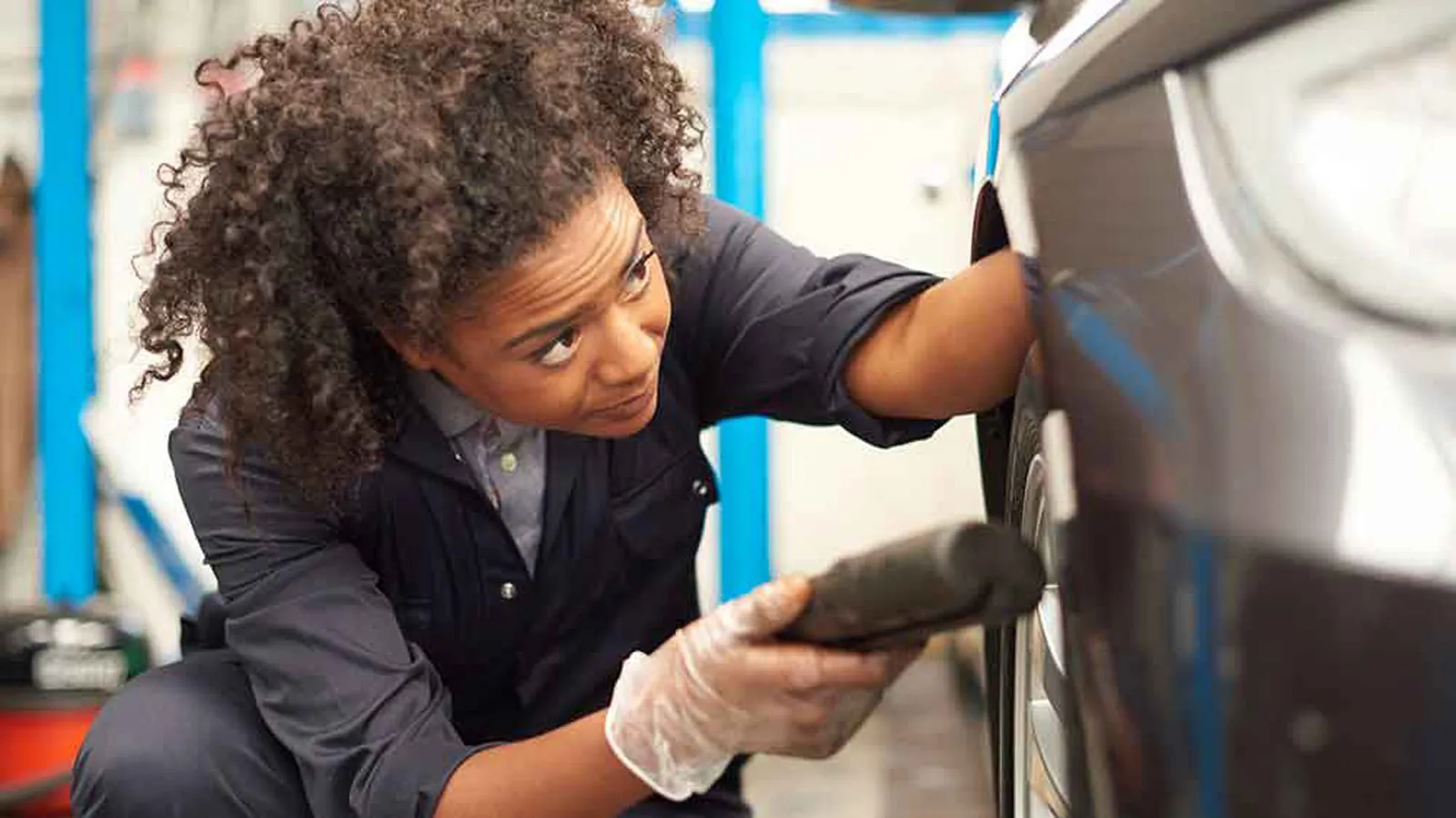 Female automotive student working on a vehicle during practical workshop training session