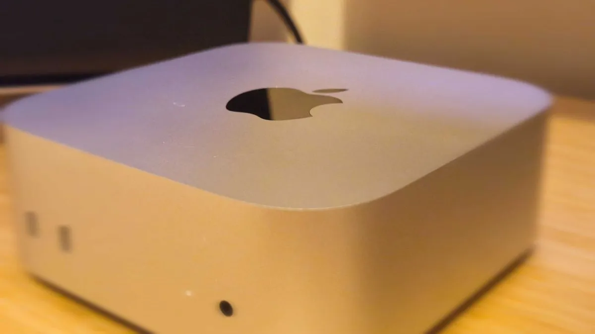 A compact silver Apple Mac mini (M4) on a wooden desk, showcasing its sleek and minimalist design
