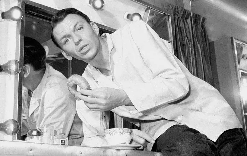 Frank Sinatra sitting elegantly with his signature glass of Jack Daniel's Tennessee Whiskey