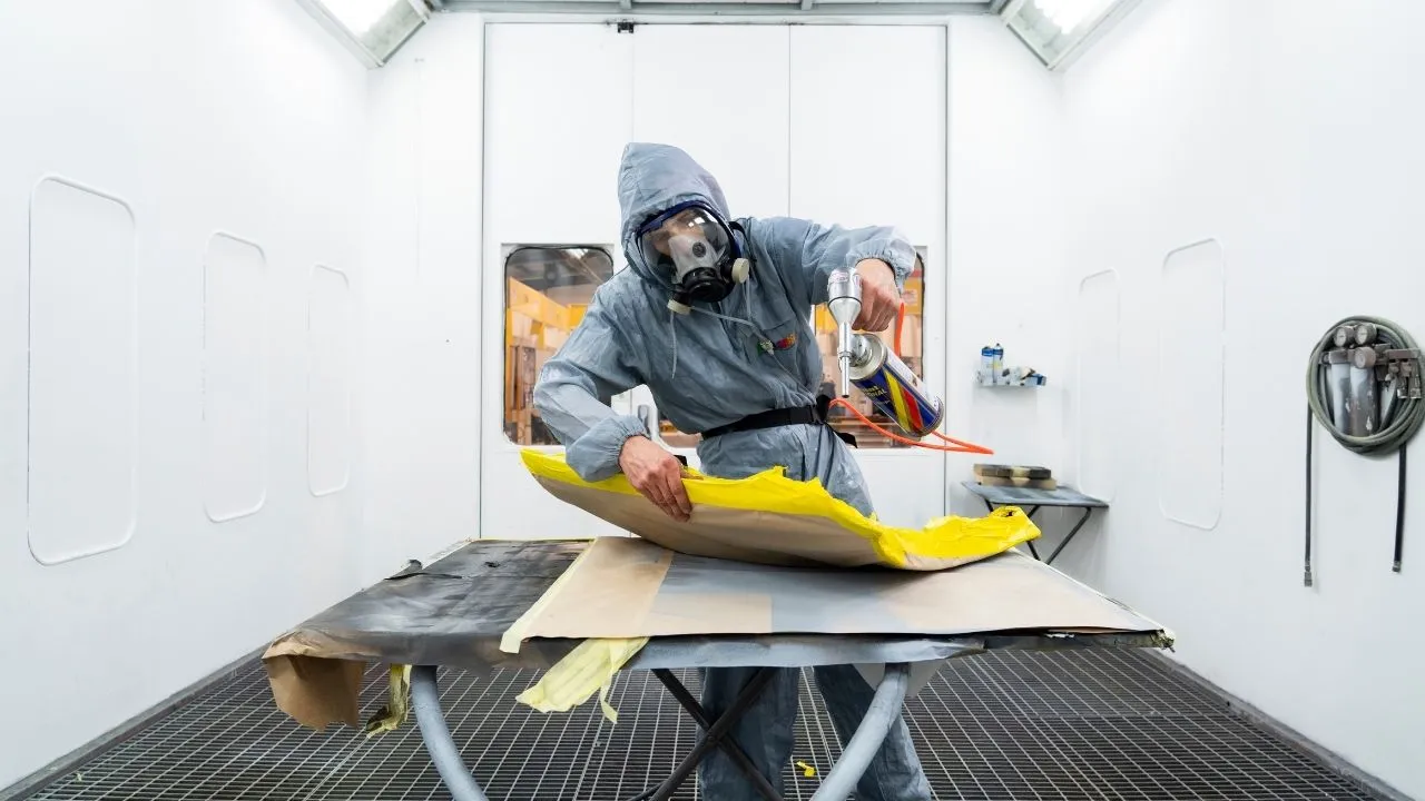 Vehicle paint booth showing student preparing car panel during spray painting practice session