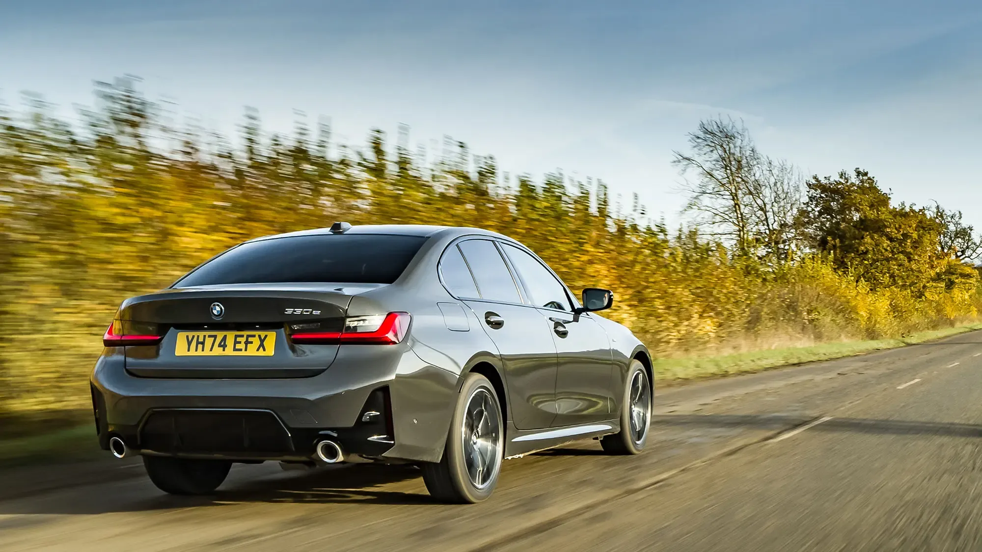 BMW 330e (2024) rear three quarter dynamic shot in grey during driving