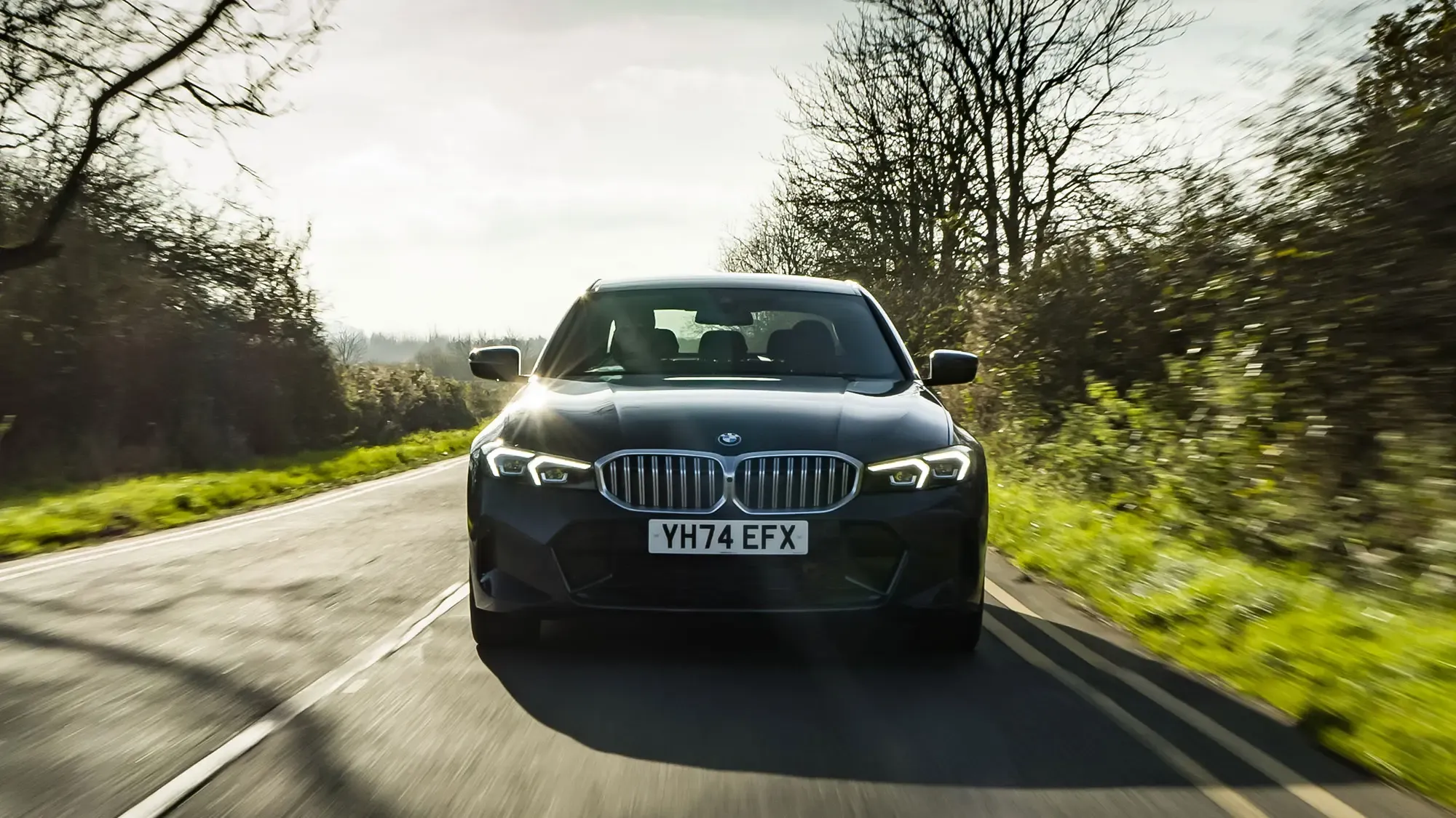 BMW 330e (2024) front view during dynamic driving on road in grey