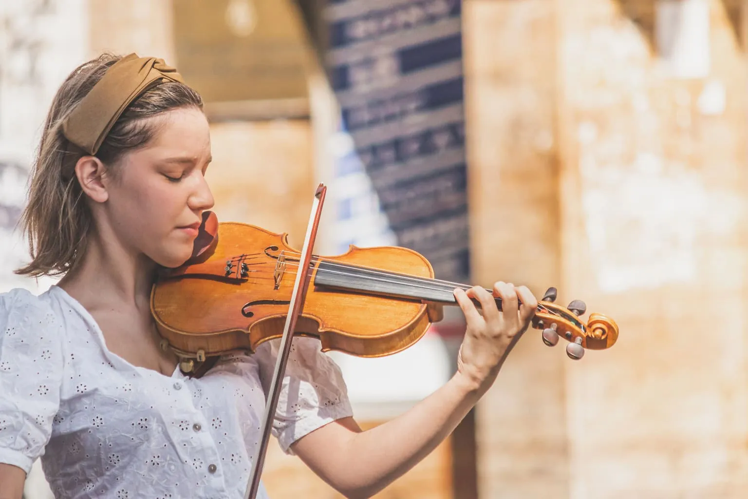 A young woman playing violin with closed eyes, fully absorbed in the music, captured in a soft portrait composition