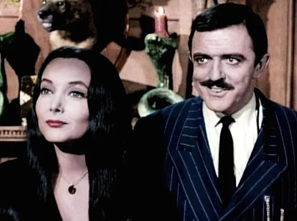 Morticia and Gomez in classic television pose at a dinner table