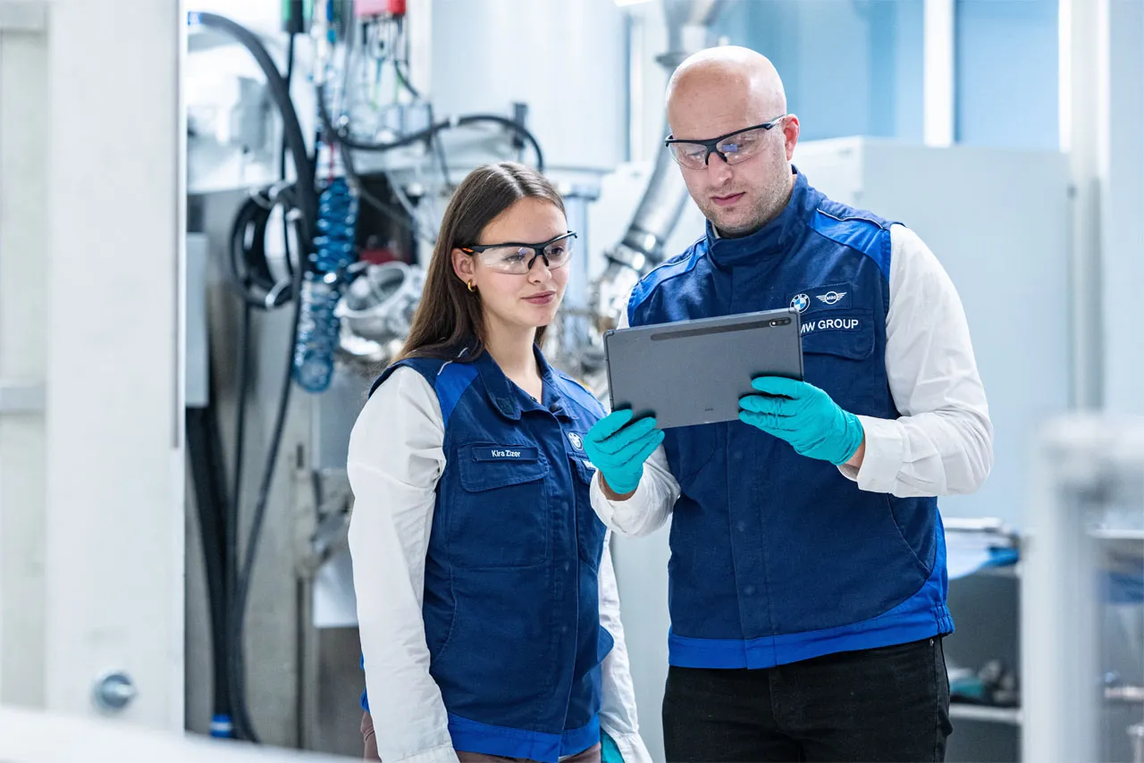 Two BMW Group employees analysing AI-supported data from battery cell production on a tablet