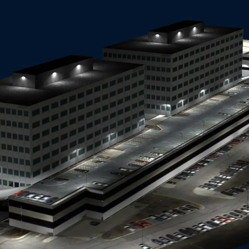 A nighttime view of two multistory office buildings with a large, well-lit parking garage and numerous parked cars, highlighting the effectiveness of photometric data in optimizing exterior lighting.