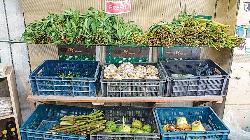 A vendor arranging freshly arrived hill vegetables including taro flowers and leafy herbs at a Dhaka market