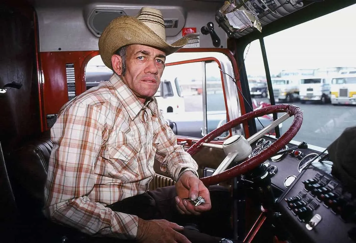 Truck driver wearing cowboy hat inside a big rig cab in 1979 highway setting