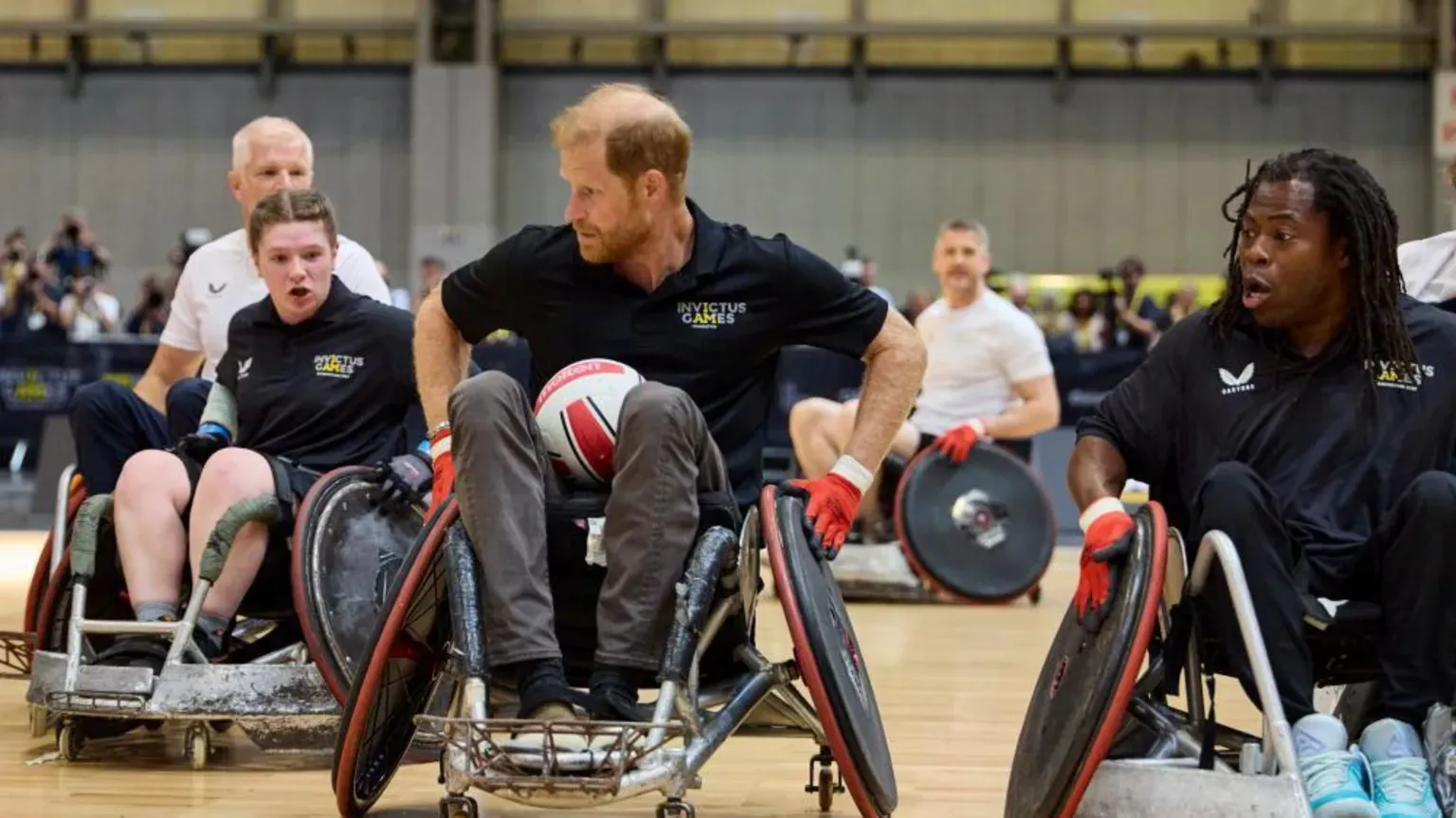 Prince Harry playing wheelchair football, sitting in a black and red wheelchair with a ball between his legs