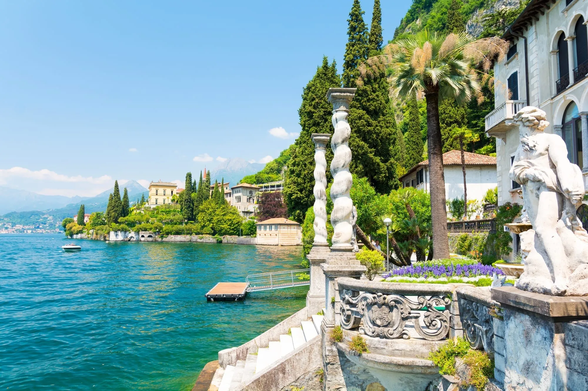 Magnificent botanical gardens of a Lake Como estate featuring vibrant spring flowers and manicured lawns leading to a stunning mountain view.