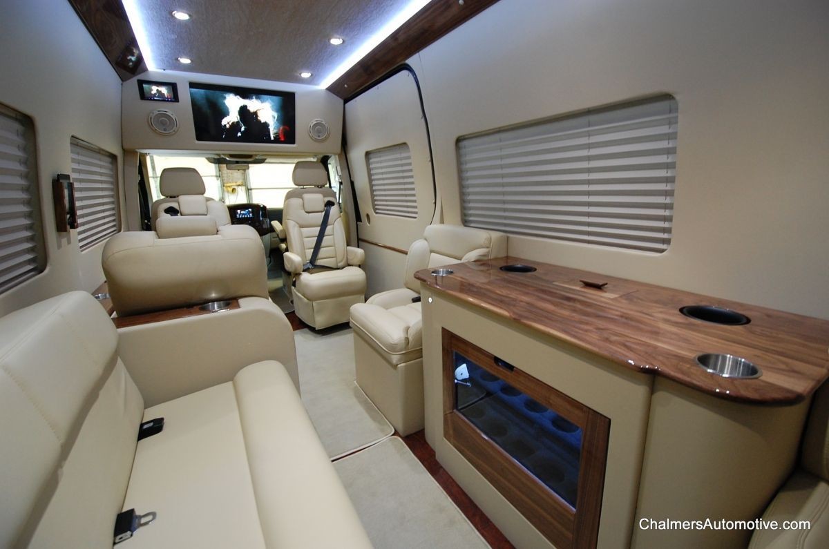 Custom luxury van cabin featuring individual passenger screens, premium audio speakers, and reclining leather seats