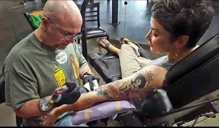 Close-up of tattoo artist integrating Elvis-themed patterns into a detailed arm sleeve design during the tattoo process