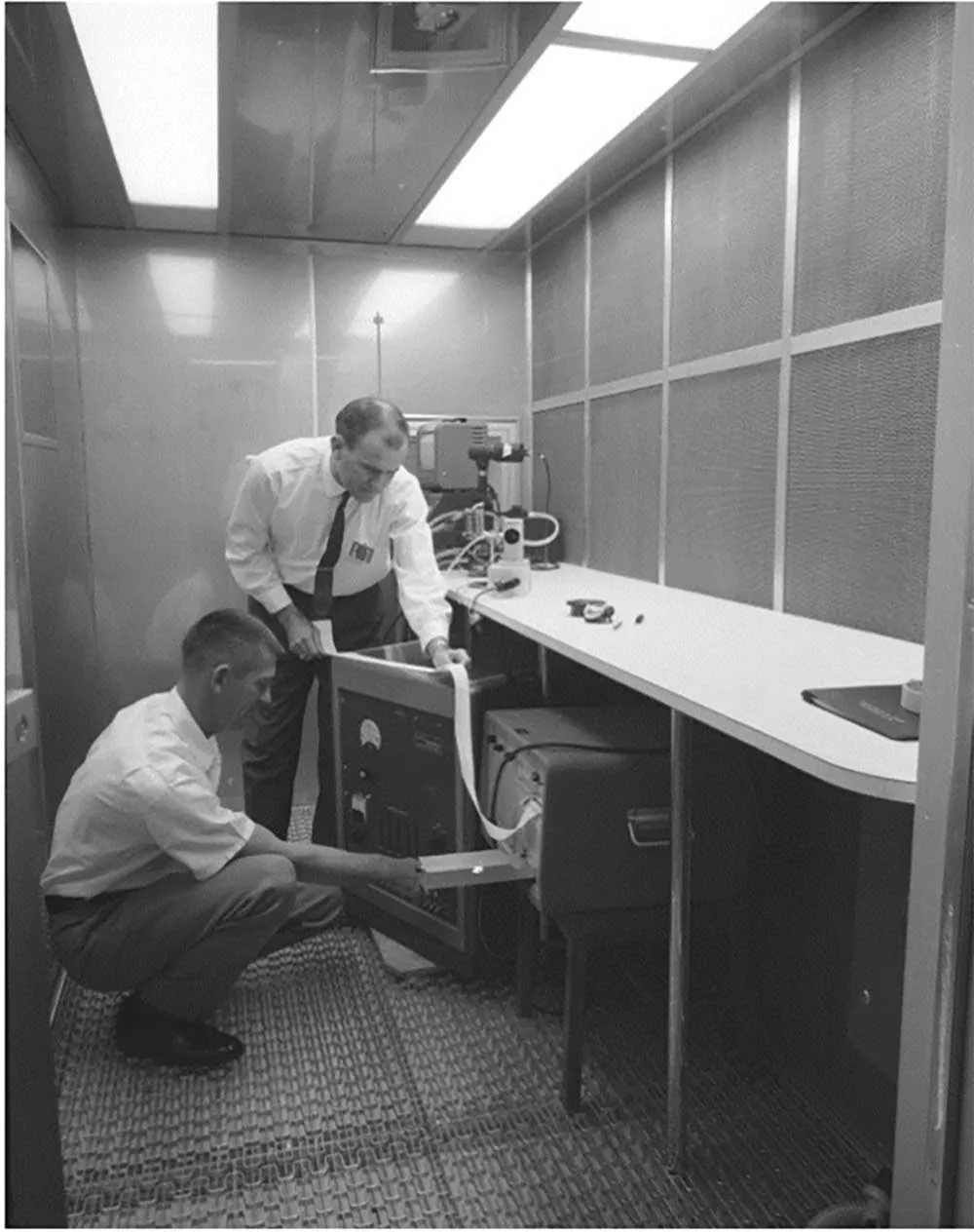 Two engineers examining equipment inside an early prototype clean room