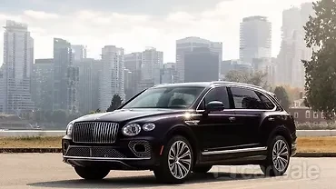 A sleek Bentley Bentayga SUV parked in a luxurious urban setting with Indian architecture in the background